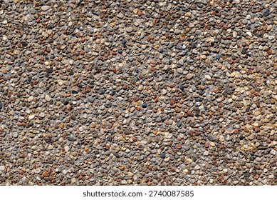 Concrete surface texture with exposed small pebbles and aggregate, rough construction material background in daylight.