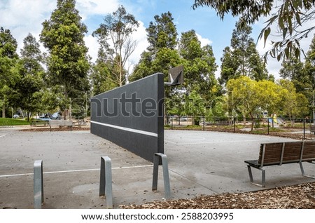 A concrete tennis practice wall and basketball court facility, the dual-purpose sports structure in a public park. Community recreational amenities in a local parkland in a suburb of Australia.