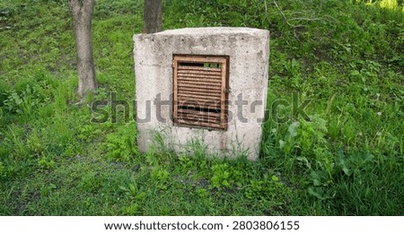 Concrete utility box with rusty vent in grassy natural area.