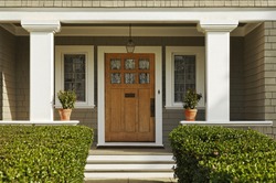 A Concrete Walkway Bordered With Hedged Shrubs Leads To The Front Door Of A Home. There Are Windows On Either Side Of The Door. Horizontal Shot.