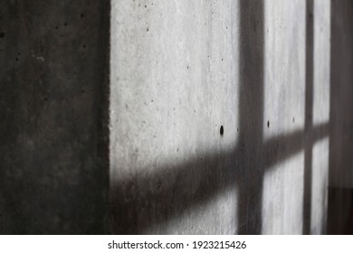 A concrete wall across from windows casting shadows of their frames. 