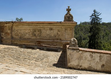 Concrete wall with baroque decoration. Old broken wall before the entrance to the castle. Balcony, view. Stone pavement. Behind the wall, out of focus, the tops of the trees and the blue sky.