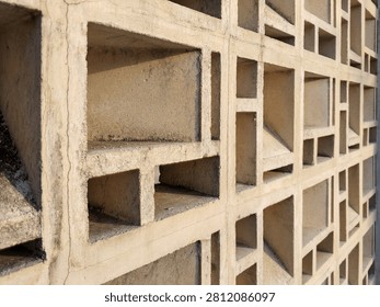 Close‑up of concrete wall with geometric grid pattern of square and rectangular recesses. Textured surface with visible cracks highlights raw architectural design. Light and shadow interplay across hollow sections, showcasing modern brutalist style, ventilation function, and structural artistry in urban construction.