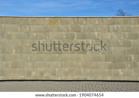 concrete wall made of smooth blocks. high dividing noise wall of the yard. under the wall is a longitudinal channel with a grid for drainage interlocking paving