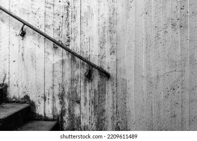 Concrete Wall And Part Of Stairs And Handrail In Gritty Black And White. No Visible People