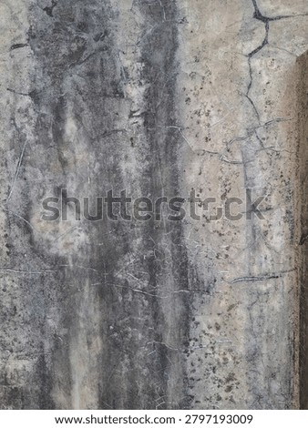 ​Gritty concrete wall texture featuring dark water running stains and cracks.