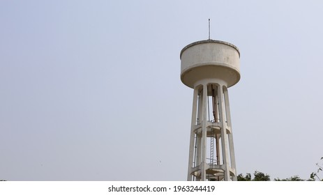 Concrete Water Tank On A Tall Tower. Large Outdoor Public White Water Tank For Village Or Urban Water Supply System On White Sky Background With Copy Space. Selective Focus