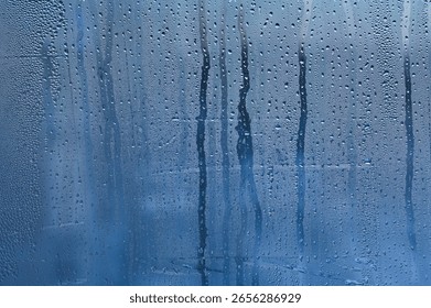 condensation, its translucent blue surface with countless micro-droplets. Some droplets grow heavy to begin their slow descent, leaving trails through fogged surface. abstract wet glass background