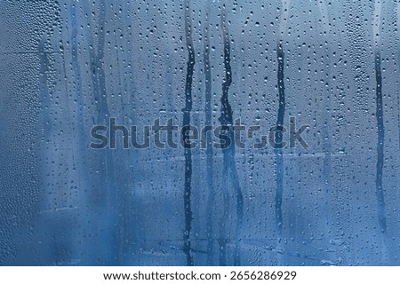 condensation, its translucent blue surface with countless micro-droplets. Some droplets grow heavy to begin their slow descent, leaving trails through fogged surface. abstract wet glass background