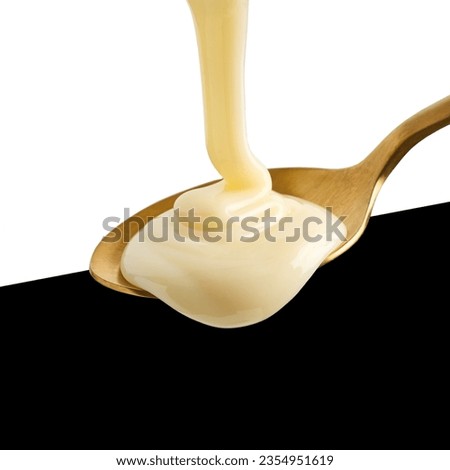 condensed milk pouring into golden spoon isolated on black and white background