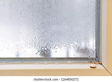 A Condensed Plastic Window With A Frame Of White Color That Has Become Foggy. Sweat On The Glass In The Kitchen Due To Changes In Temperature, Small Drops Of Water On The Window In Winter