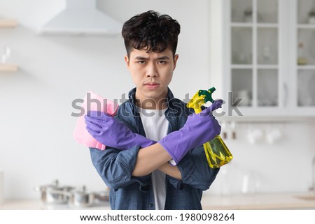 Condifent asian man with spray bottle and dust cloth as with guns seriously looking at camera. Motivated korean guy cleaning kitchen, wearing gloves, copy space. House-keeping concept