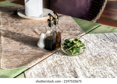 A Condiment Set Is Set On The Wooden Table With The Shadow Of The Bottle Lay Down On The Table Cloth.