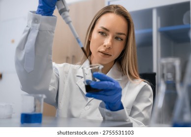 Conducting meticulous sample transfer using a pipette to add dark biological liquid into beaker at laboratory workstation.