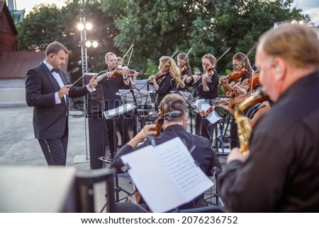 Conductor directing orchestra performance on outdoor stage