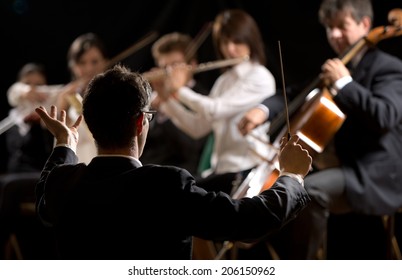 Conductor Directing Symphony Orchestra With Performers On Background.