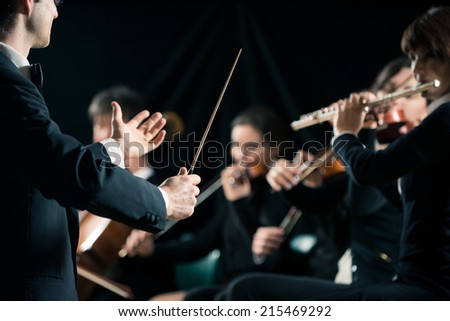Conductor directing symphony orchestra with performers on background.