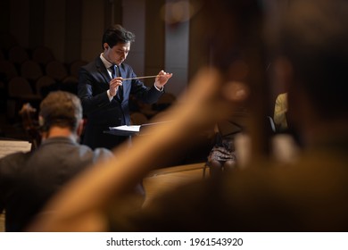 Conductor Of Symphony Orchestra With Performers In Background In Concert Hall