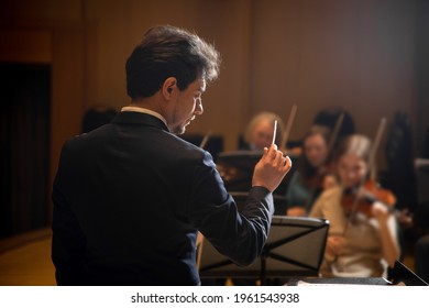 Conductor Of Symphony Orchestra With Performers In Background In Concert Hall