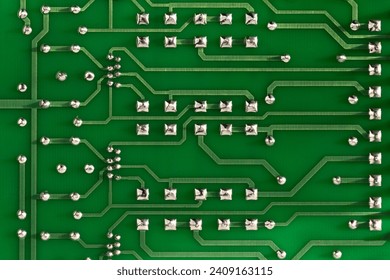 Conductor traces with silver drops of solder on a green electronic circuit. Computer board with electrically conductive circuits of an electronic circuit in the form of stripes close-up.