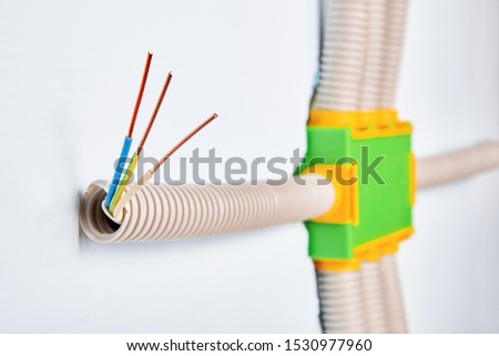 The conduit is connected to the electrical distribution box of the household wiring, the ends of the bare copper wires are visible from the outside of the pipe. Installation of a electric panel.