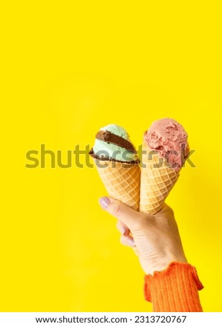 A cone of refreshing ice cream in a waffle cup against a yellow wall. Selective focus, noise. The concept of vacation, vacation at sea. A woman holds ice cream in her hands. Vertical photo