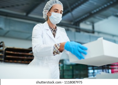 Confectionery factory employee standing in white coat and holding paper package box.