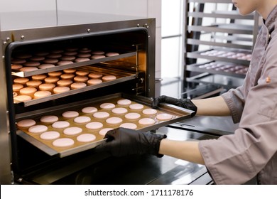 Confectionery preparation precess. Confectioner woman lays a batch of cakes macaron in the oven. - Shutterstock ID 1711178176