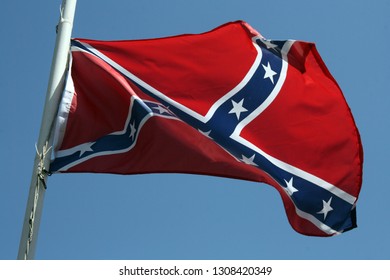 Confederate Flag Flying At Half Mast Against A Blue Sky Background