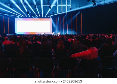 Conference audience facing a bright screen with vivid blue and orange stage lights - Powered by Shutterstock