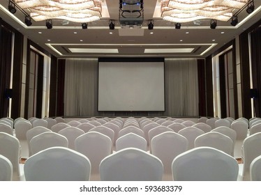 Conference Meeting Room With Ceiling LED Lights, Row Of White Chairs, With Stage And Empty Screen For Business Meeting, Conference, Training Course, Used As Template Of The Elegant Design Office