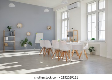 Conference Room For Business Meetings. Empty Interior Of Beautiful Modern Minimalist Office With White Table, Comfortable Chairs, Whiteboard, Shelves, Indoor Plants And Large Plastic Windows