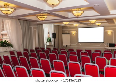 Conference Room With Red Chairs, Interior Lighting, And Empty White Insulated Screen. Business Meetings, Conferences, Trainings, Used As Template For Elegant Design. Interior Of The Conference Hall