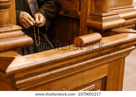a confessional where a Catholic priest sits and confesses the faithful. Focus on the hands of the priest praying the rosary