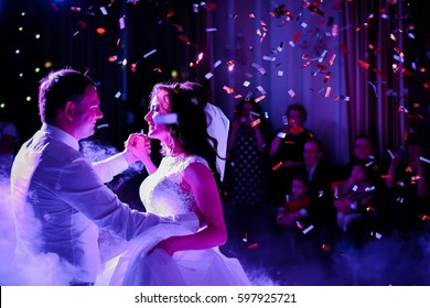 Confetti fall on wedding couple whirling in the smoke