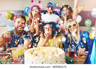 Confetti flying around group celebrating a party with large cake and drinks on table in front of them - Shutterstock ID 489082672