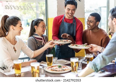 Confidant waiter serving delicious pizzas margherita to multicultural friends in cozy pizzeria restaurant - Multiethnic friends having fun together at the pizzeria eating pizza and drinking blond beer