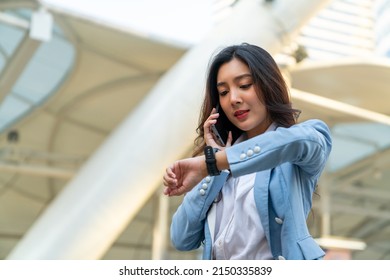 Confidence Asian businesswoman checking time on hand watch while walking in city street. Business woman working busy talking on mobile phone for online corporate business at office building district - Powered by Shutterstock