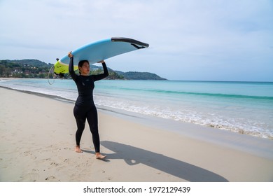 Confidence Asian Woman In Wetsuit Holding Surfboard And Walking On Tropical Beach At Summer Sunny Day. Healthy Sportswoman Enjoy Outdoor Active Lifestyle Play Extreme Sport Surfing On Summer Vacation