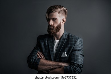 Confidence And Charisma. Attractive Young Man Keeping Arms Crossed And Looking Away While Standing Against Grey Background