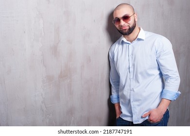 Confidence and charisma. Handsome young latin man holding hands in pockets and looking at camera while leaning on grey wall.