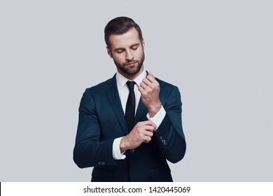 Confidence and charisma. Handsome young man adjusting his sleeve while standing against grey background