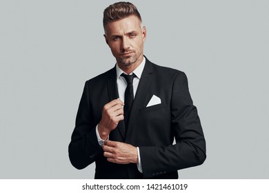 Confidence And Charisma. Handsome Young Man Adjusting His Sleeve While Standing Against Grey Background