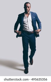 Confidence In Every Move. Full Length Of Handsome Young African Man In Full Suit Adjsuting His Jacket While Walking Ahead And Being In Front Of Grey Background