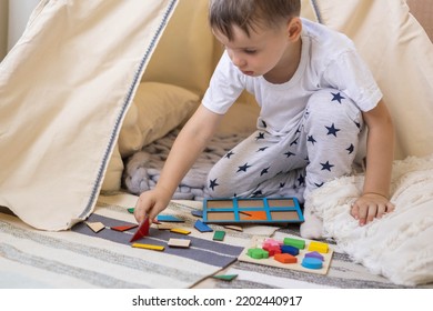 Confidence male kid in pajamas assembling geometric form shape on wooden board cells at fabric wigwam childish room. Cute baby boy playing eco material early development logic elementary education - Shutterstock ID 2202440917