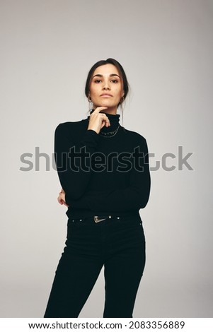 Confidence personified. Fashionable young woman looking at the camera while standing alone against a grey background. Self-confident young woman posing in a studio.