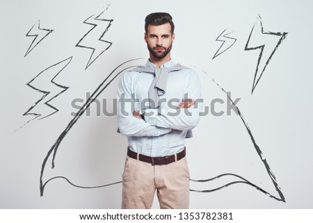 Confidence and power. Charming bearded man wearing a drawn cape with crossed arms is looking at camera while standing against grey background with illustration of the lightning bolts