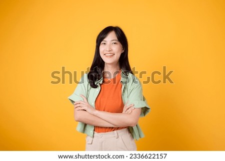 confidence and well-being with a young 30s Asian woman in her wearing an orange shirt. Her arm cross gesture on her chest against a vibrant yellow background emanates self-assuredness and inner peace.