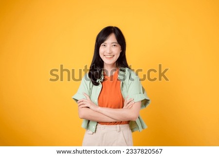 confidence and well-being with a young 30s Asian woman wearing an orange shirt. Her arm cross gesture on her chest against a yellow background evokes a portrait of self-assuredness and inner peace.