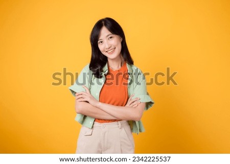 confidence and well-being with a young 30s Asian woman wearing an orange shirt. Her arm cross gesture on her chest against a vibrant yellow background radiates self-assuredness and inner peace.